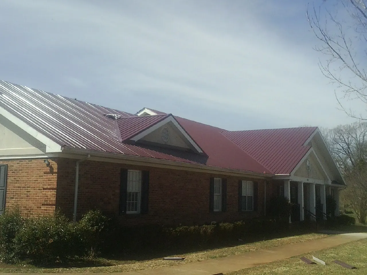 Red metal roof with gabled entries on a long brick building, from a Hail Damage Roof Repair job in Englewood