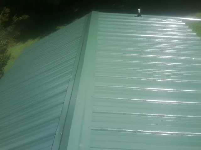 New green metal panels meeting at the ridge of a roof — Flat Roof Repair work by our crew in Englewood