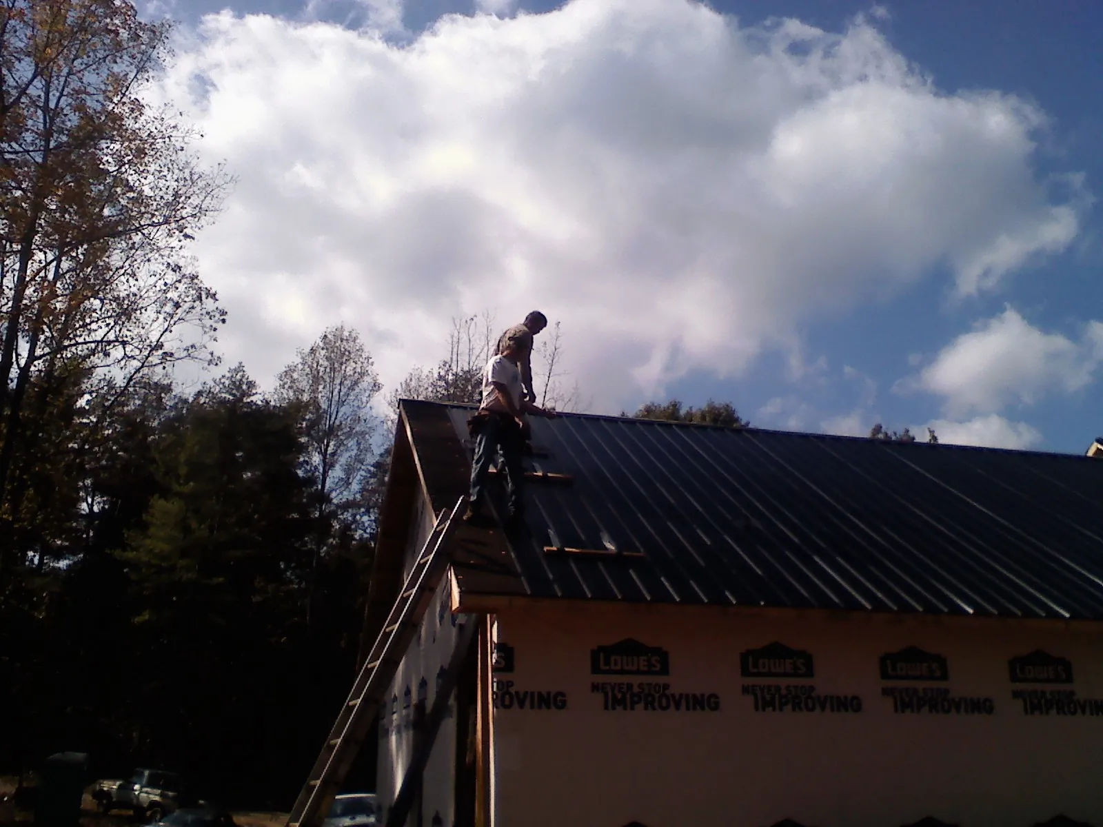 Roofer fastening dark metal panels high against a cloudy sky, from a Roof Inspection job in Englewood