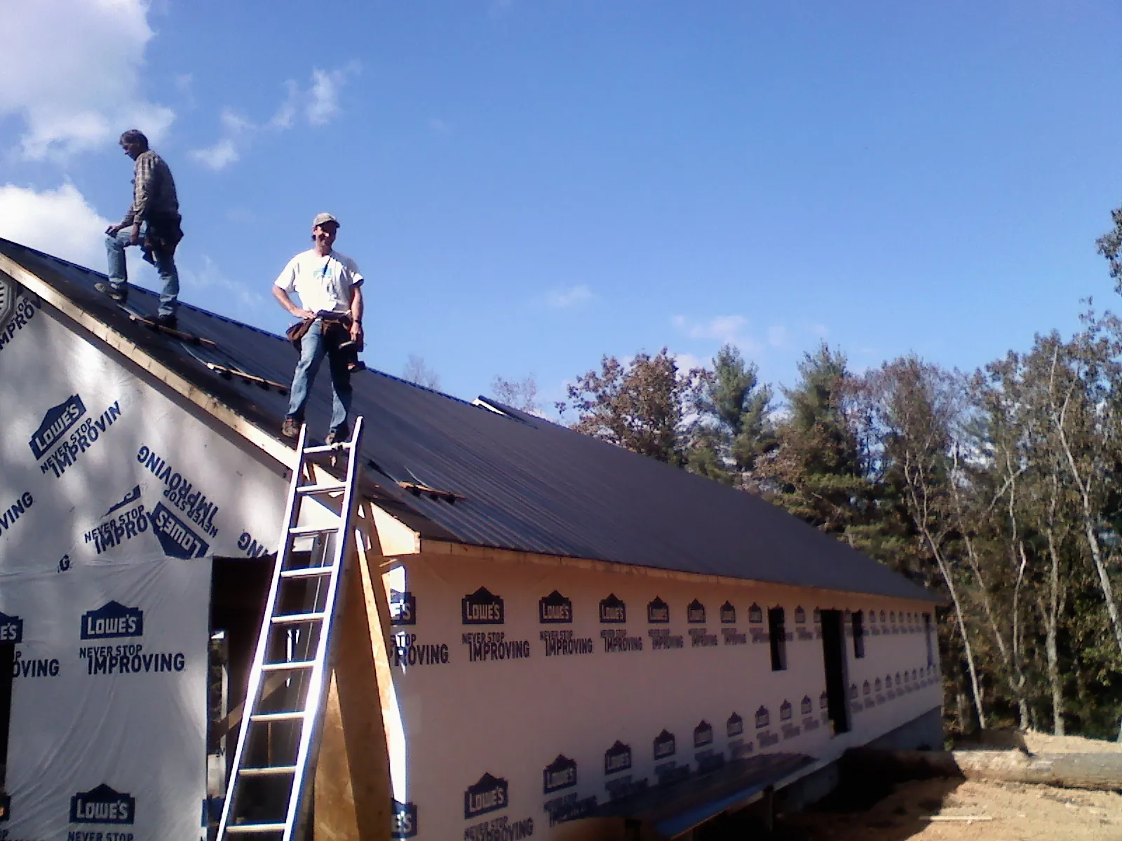 Two roofers standing on a long dark metal roof over a wrapped building in Englewood